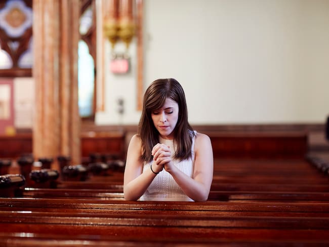 Mujer orando en una iglesia (GettyImages)
