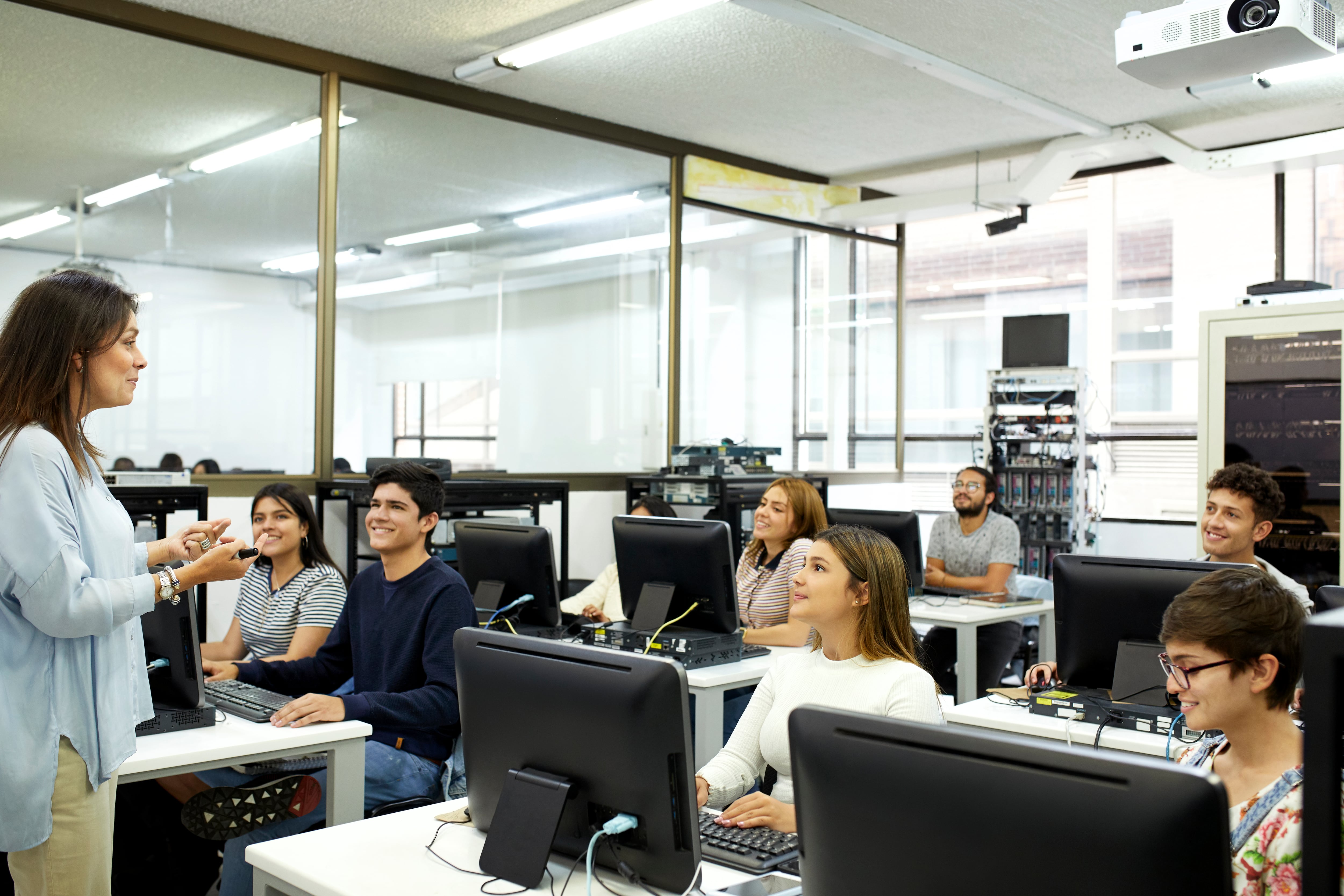 Profesora explicándole un tema a sus estudiantes en salón de tecnología (Foto vía Getty Images)