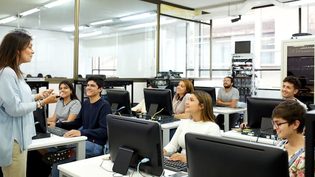 Profesora explicándole un tema a sus estudiantes en salón de tecnología (Foto vía Getty Images)
