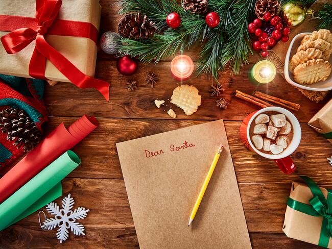 Vista superior de la carta de Navidad y el material para envolver regalos de Navidad en una mesa de madera rústica. Getty Images