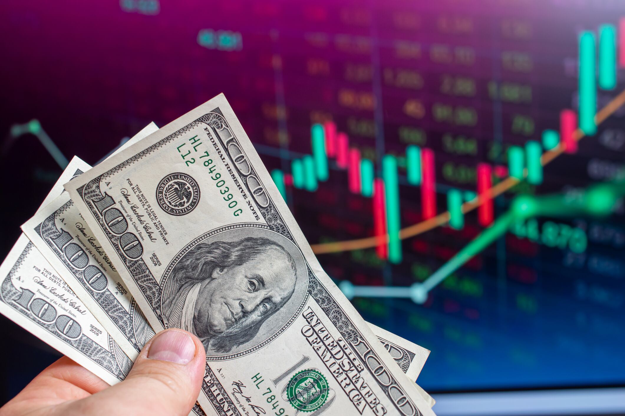 Dólares en la mano de una persona con un fondo de las gráficas sobre los indicadores económicos (Getty Images)