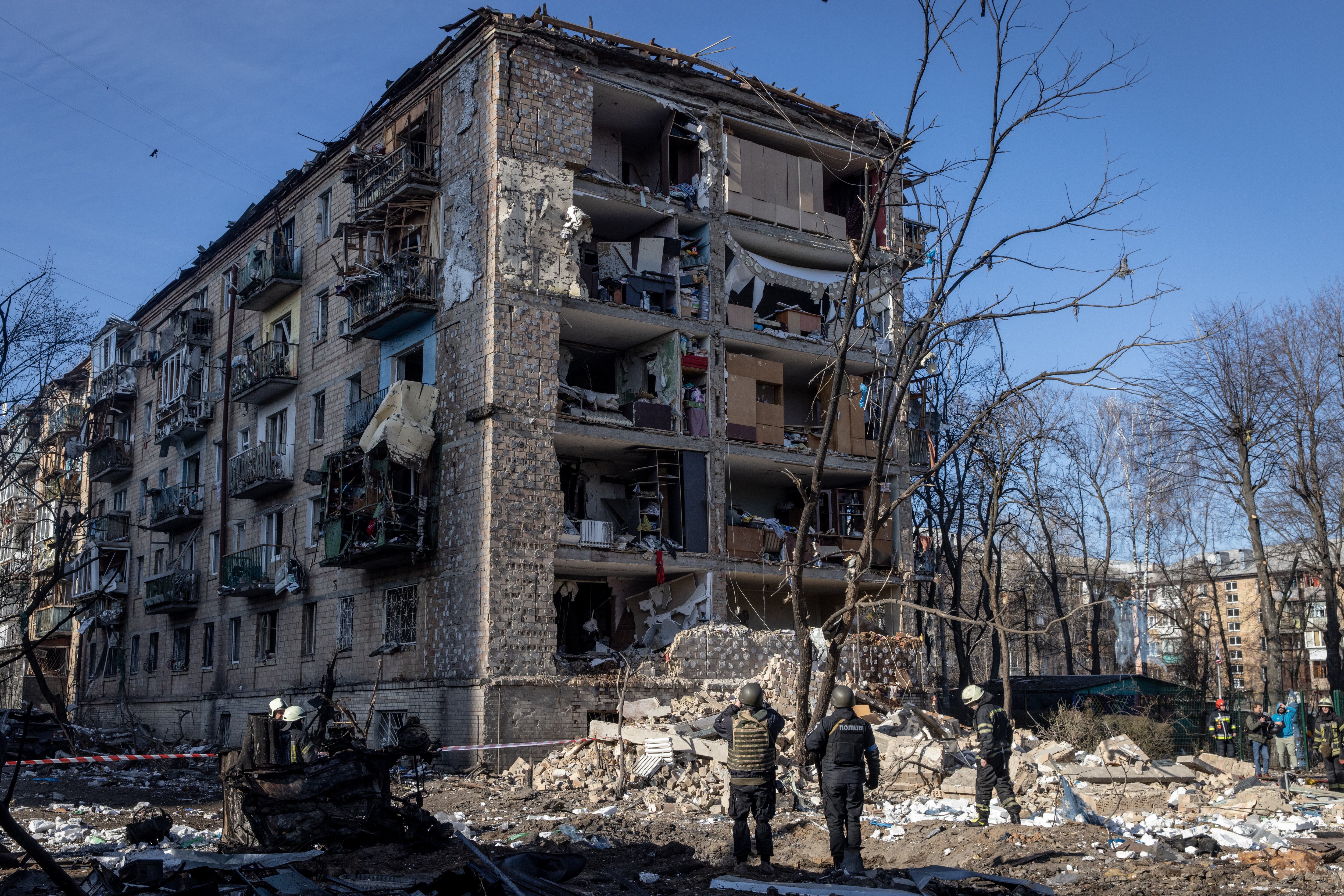 KYIV, UKRAINE - MARCH 18: Police and military personnel stand in front of a residential apartment complex that was heavily damaged by a Russian attack on March 18, 2022 in Kyiv, Ukraine. Russian forces remain on the outskirts of the Ukrainian capital, but their advance has stalled in recent days, even while Russian strikes - and pieces of intercepted missiles - have hit residential areas in the north of Kyiv. An estimated half of Kyiv's population has fled to other parts of the country, or abroad, since Russia invaded on February 24. (Photo by Chris McGrath/Getty Images)