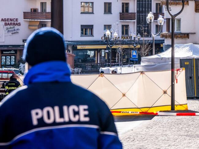 A police officer patrols on front of folding screens set up around the Constellation bar in the luxury Alpine ski resort town of Crans-Montana, on January 1, 2026 after a fire ripped through the venue during the New Year's Eve celebrations. Several dozen people are presumed dead and around 100 injured after a fire ripped through a crowded bar in the luxury Swiss ski resort of Crans-Montana, Swiss police said on January 1, 2026. Police, firefighters and rescuers rushed to the popular resort, which is set to host the Ski World Cup from January 30, after the fire broke out in the early hours of New Year's Day. (Photo by MAXIME SCHMID / AFP)