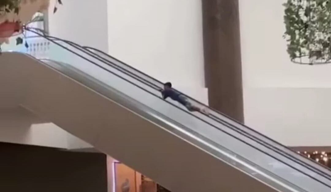 Menor subiendo las escaleras eléctricas por el pasamanos. 