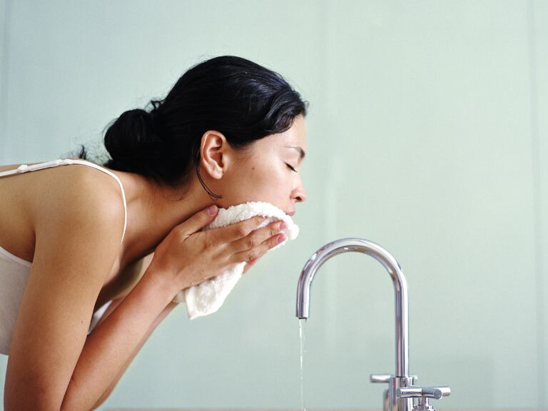 Mujer lavándose la cara y secándose el rostro con una toalla (Getty Images)