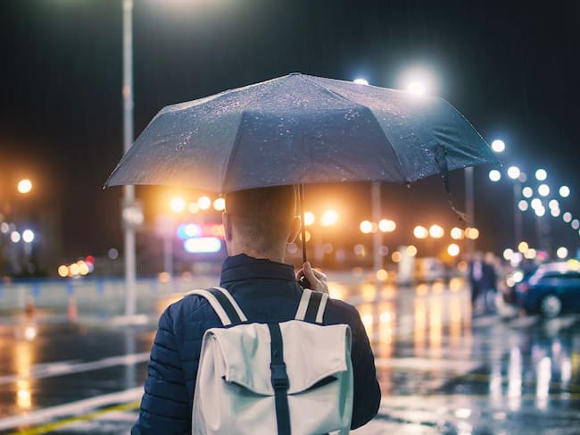 Un hombre sosteniendo un paraguas mojado en una calle de la ciudad bajo la lluvia, por la noche. - Foto Getty Images