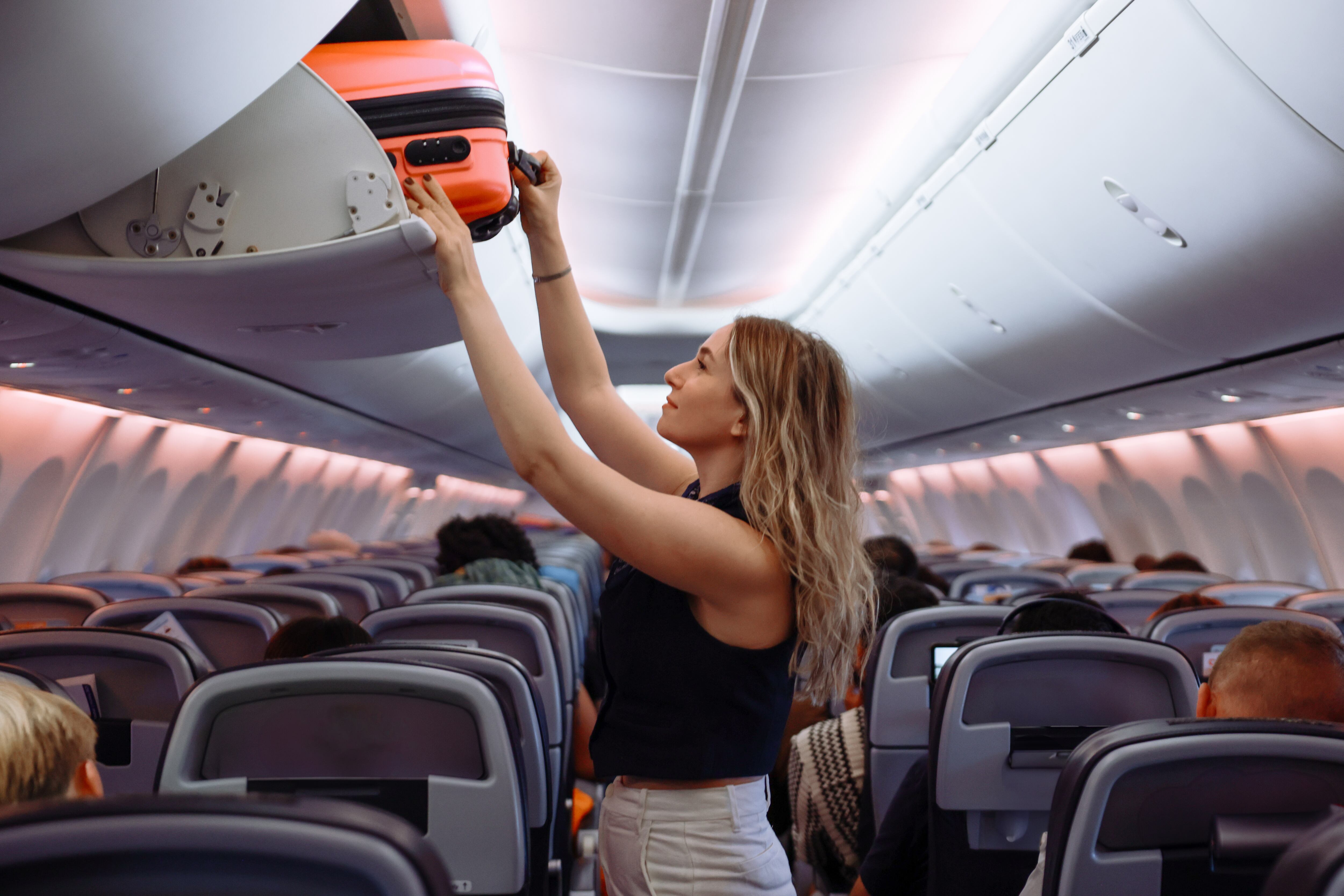Woman travel by airplane. Passenger putting hand baggage in lockers above seats of plane. hands are seen placing or retrieving a pink hard-shell suitcase from an airplane's overhead storage compartment.