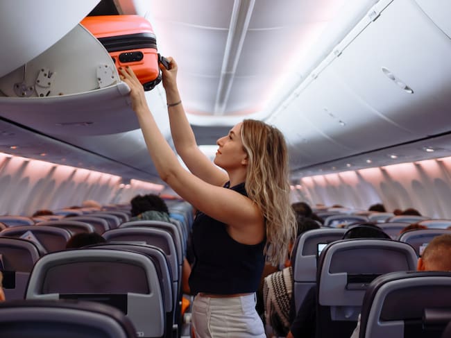 Woman travel by airplane. Passenger putting hand baggage in lockers above seats of plane. hands are seen placing or retrieving a pink hard-shell suitcase from an airplane's overhead storage compartment.
