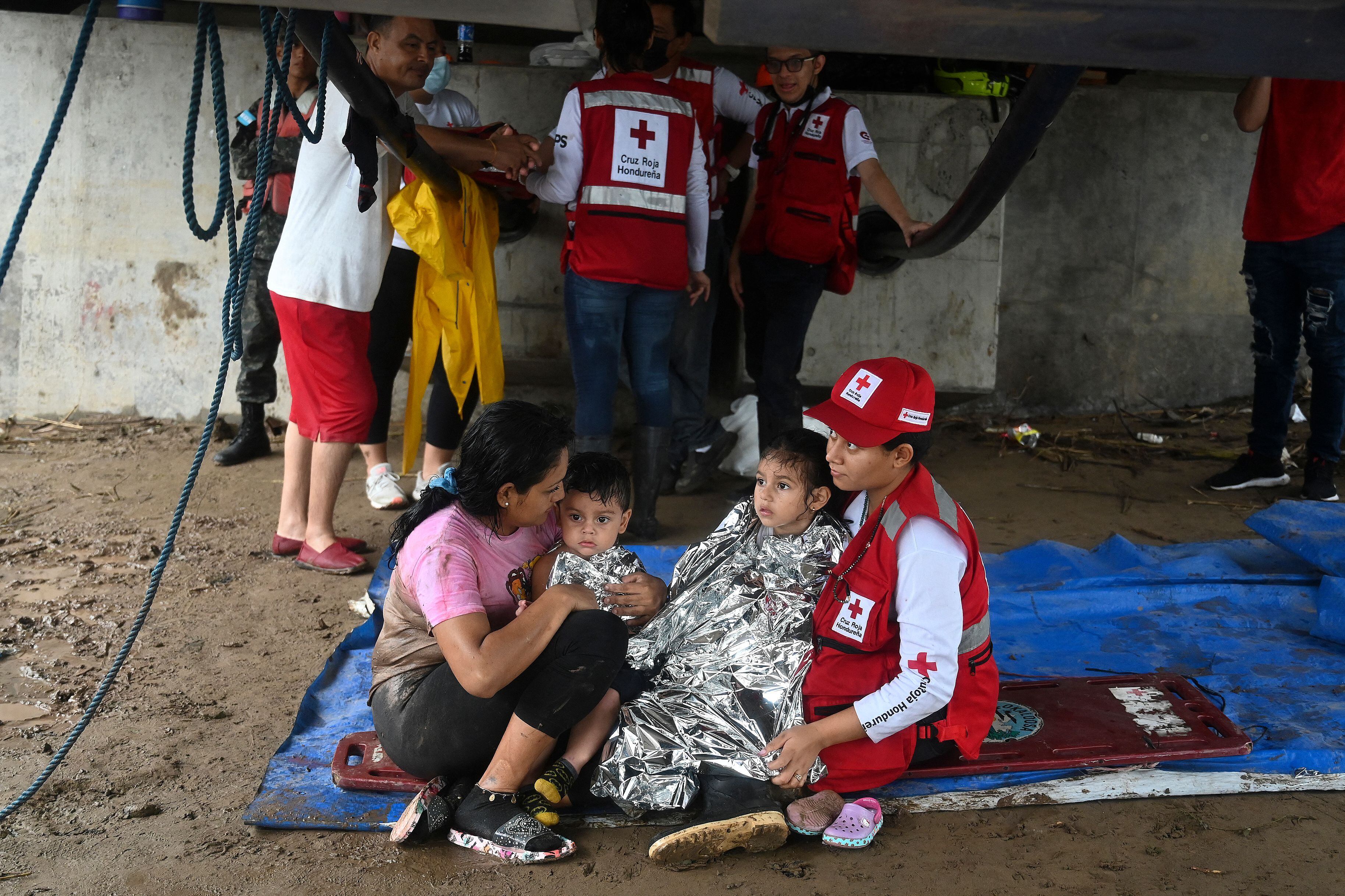 A woman and her two children is helped by a member of the Honduran red cross after the overflow of the Ulua river in El Progreso, Honduras, on September 24, 2022. - Honduras declared a red alert in the northwestern region of the country due to the scourge of torrential rains that caused the overflow of rivers, leaving at least 13 dead during the last week and more than 200 houses destroyed by landslides in the Honduran capital. (Photo by Orlando SIERRA / AFP) (Photo by ORLANDO SIERRA/AFP via Getty Images)
