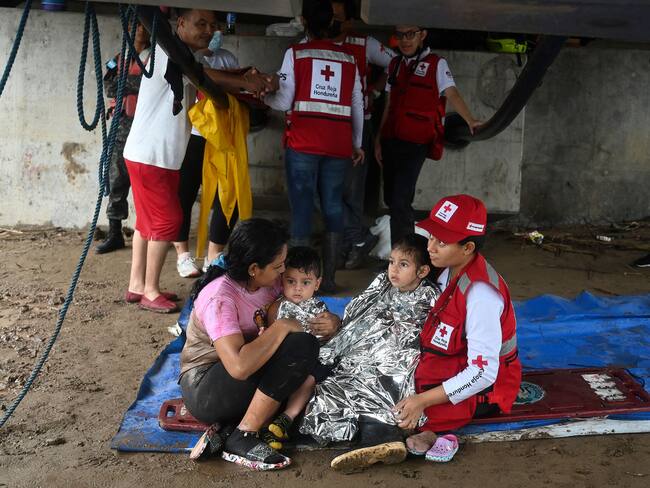 A woman and her two children is helped by a member of the Honduran red cross after the overflow of the Ulua river in El Progreso, Honduras, on September 24, 2022. - Honduras declared a red alert in the northwestern region of the country due to the scourge of torrential rains that caused the overflow of rivers, leaving at least 13 dead during the last week and more than 200 houses destroyed by landslides in the Honduran capital. (Photo by Orlando SIERRA / AFP) (Photo by ORLANDO SIERRA/AFP via Getty Images)