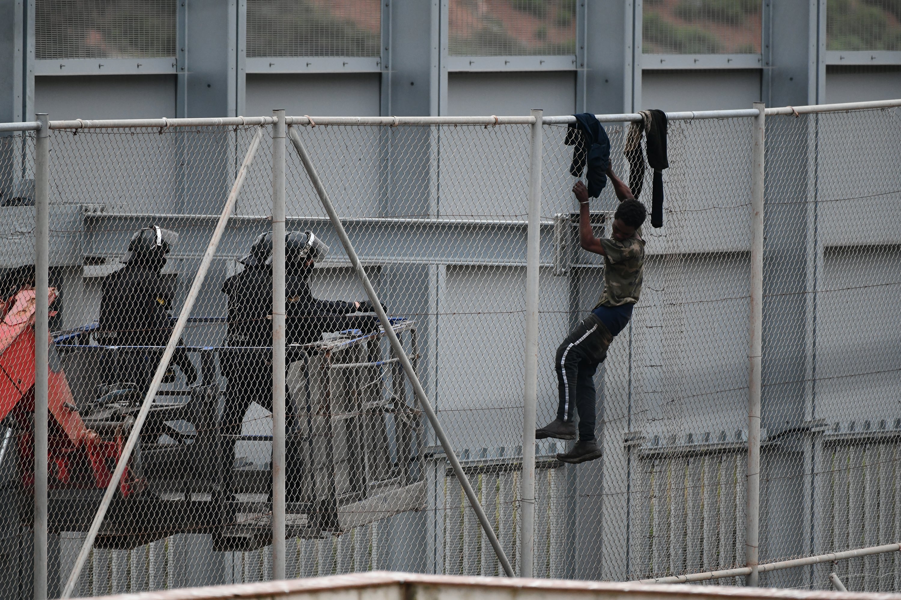 Dos agentes se acercan a un migrante que intenta saltar la reja que separa Ceuta (España) de Marruecos.
(Foto: Antonio Sempere/Europa Press via Getty Images)