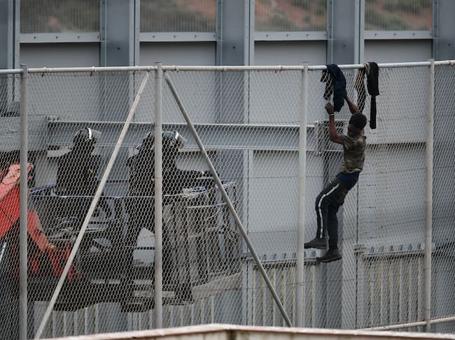Dos agentes se acercan a un migrante que intenta saltar la reja que separa Ceuta (España) de Marruecos.
(Foto: Antonio Sempere/Europa Press via Getty Images)