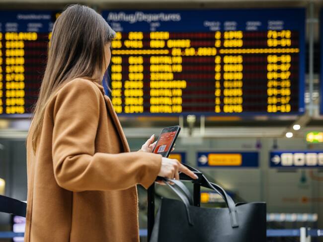A woman traveler checks her mobile phone in front of the airport's flight information board, preparing for her upcoming solo journey.