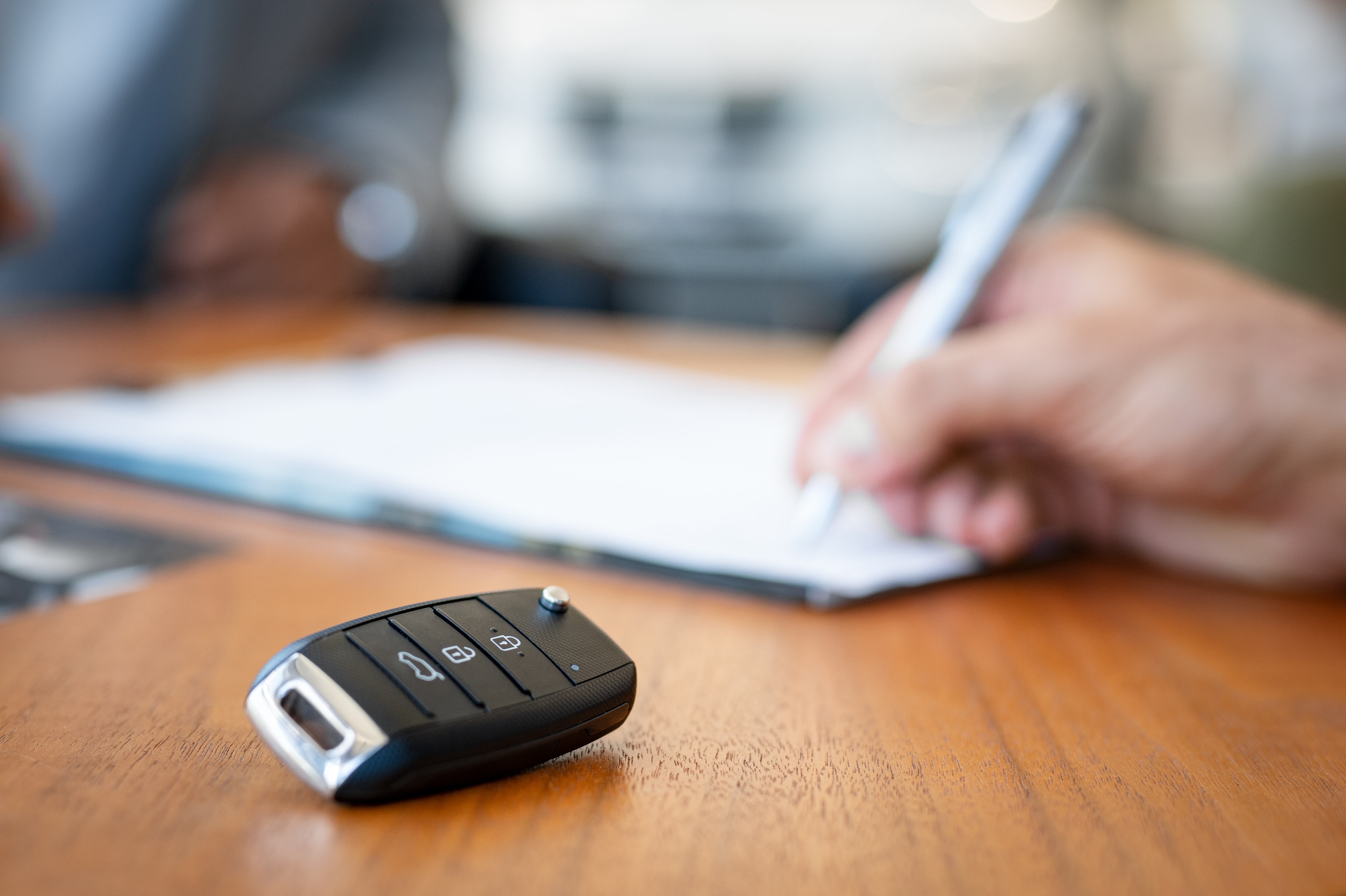 Persona firmando un documento con unas llaves de un carro al lado (Foto vía Getty Images)
