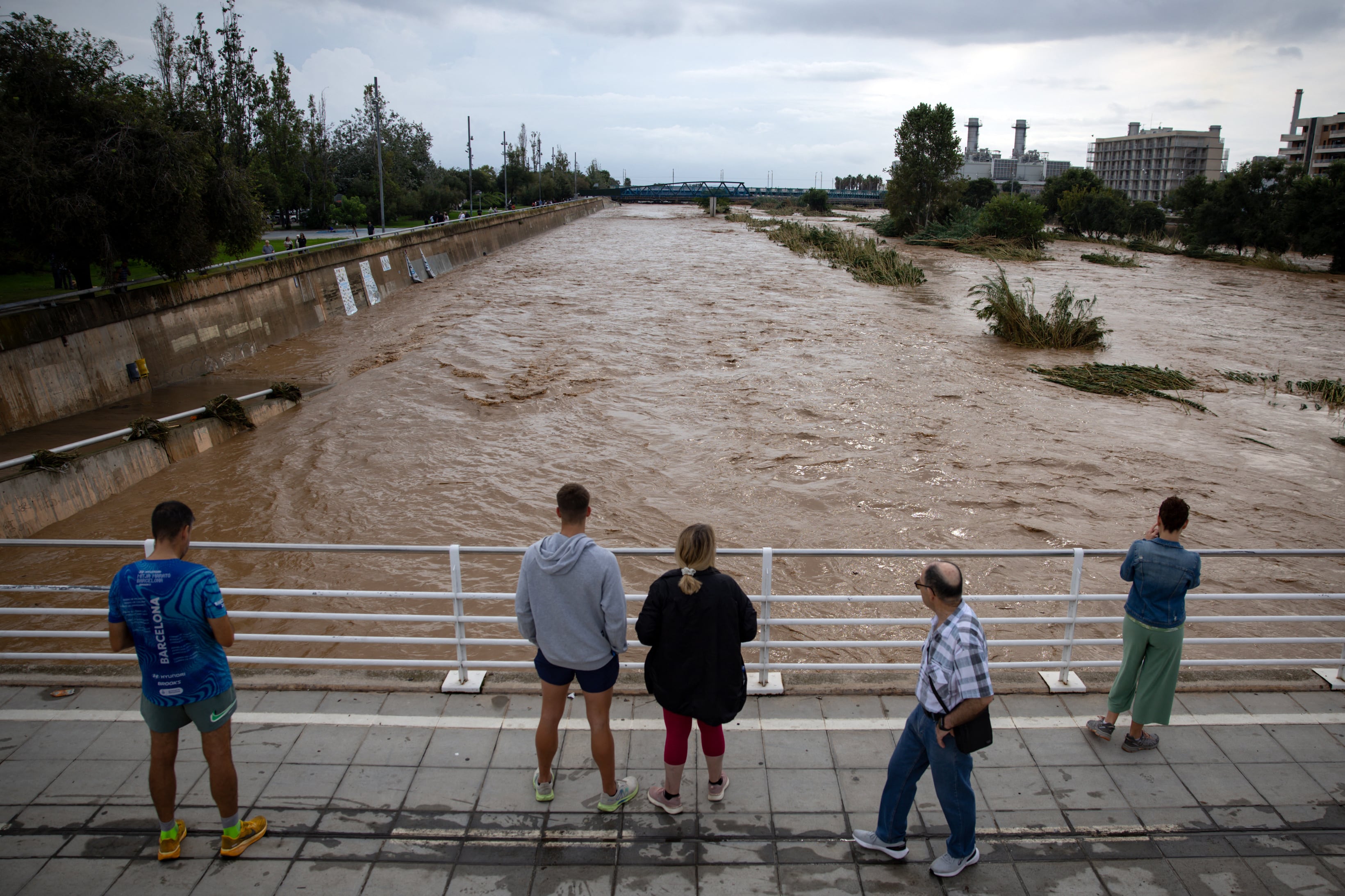 People watch the swollen Besos River following torrential rains in Sant Adria de Besos, on the outskirts of Barcelona, on October 4, 2026. Torrential rains battering eastern Spain have left two dead and kept the city of Barcelona and its surrounding areas on high alert, authorities said today, warning of the risk of flooding and overflowing rivers. (Photo by Josep LAGO / AFP)