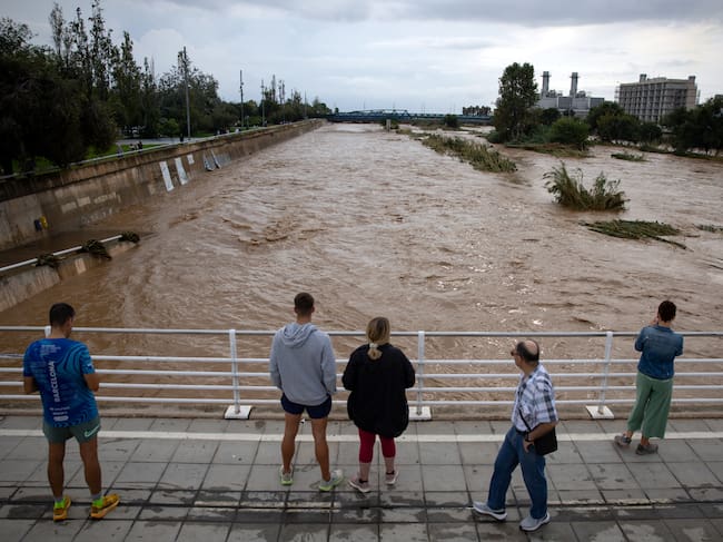 People watch the swollen Besos River following torrential rains in Sant Adria de Besos, on the outskirts of Barcelona, on October 4, 2026. Torrential rains battering eastern Spain have left two dead and kept the city of Barcelona and its surrounding areas on high alert, authorities said today, warning of the risk of flooding and overflowing rivers. (Photo by Josep LAGO / AFP)