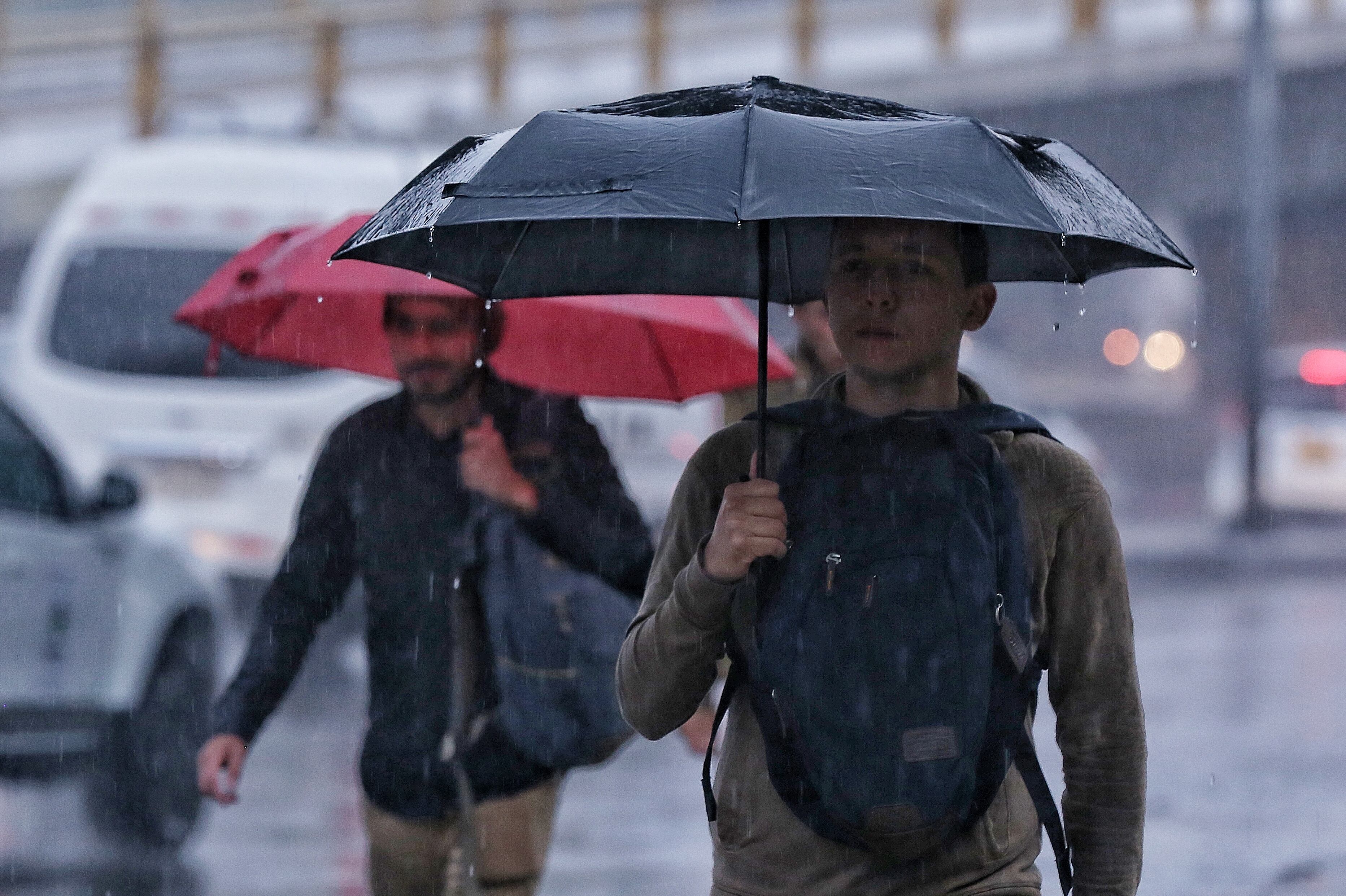 Personas caminando con sombrilla por Bogotá mientras llueve. (Foto vía COLPRENSA)