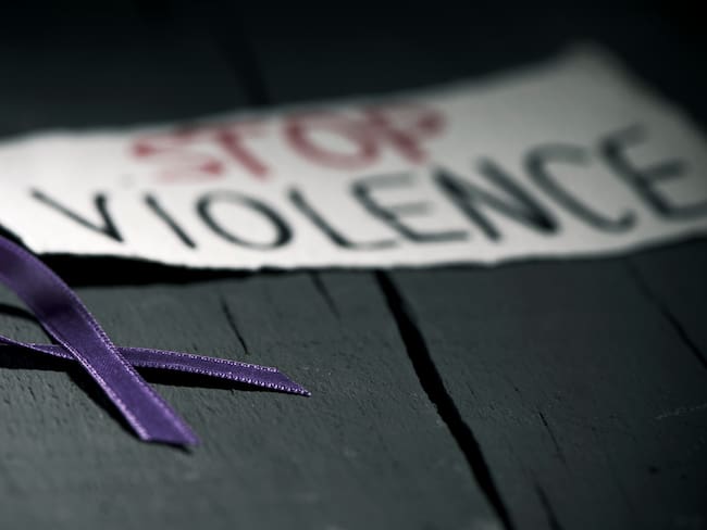 a purple ribbon for the awareness about the unacceptability of the violence against women and the text stop violence on a piece of paper, on a dark gray rustic wooden surface