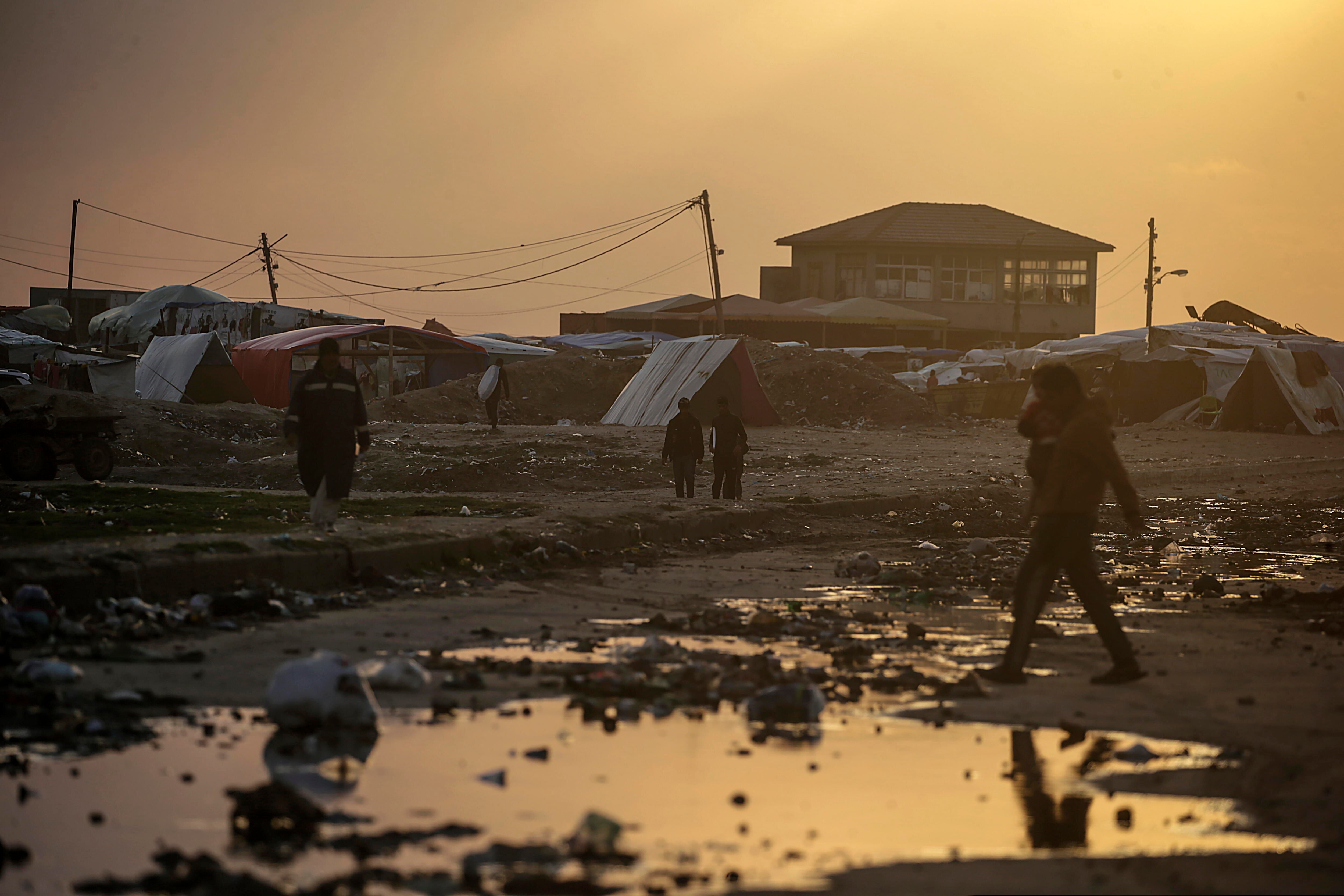 Deir Al Balah (---), 30/01/2024.- Displaced Palestinians who fled their houses from the northern Gaza Strip walk past a rain water puddle next to their shelters during a cold evening in Deir Al Balah town, southern Gaza Strip, 30 January 2024. More than 26,700 Palestinians and at least 1,330 Israelis have been killed, according to the Palestinian Health Ministry and the Israel Defense Forces (IDF), since Hamas militants launched an attack against Israel from the Gaza Strip on 07 October 2023, and the Israeli operations in Gaza and the West Bank which followed it. EFE/EPA/MOHAMMED SABER