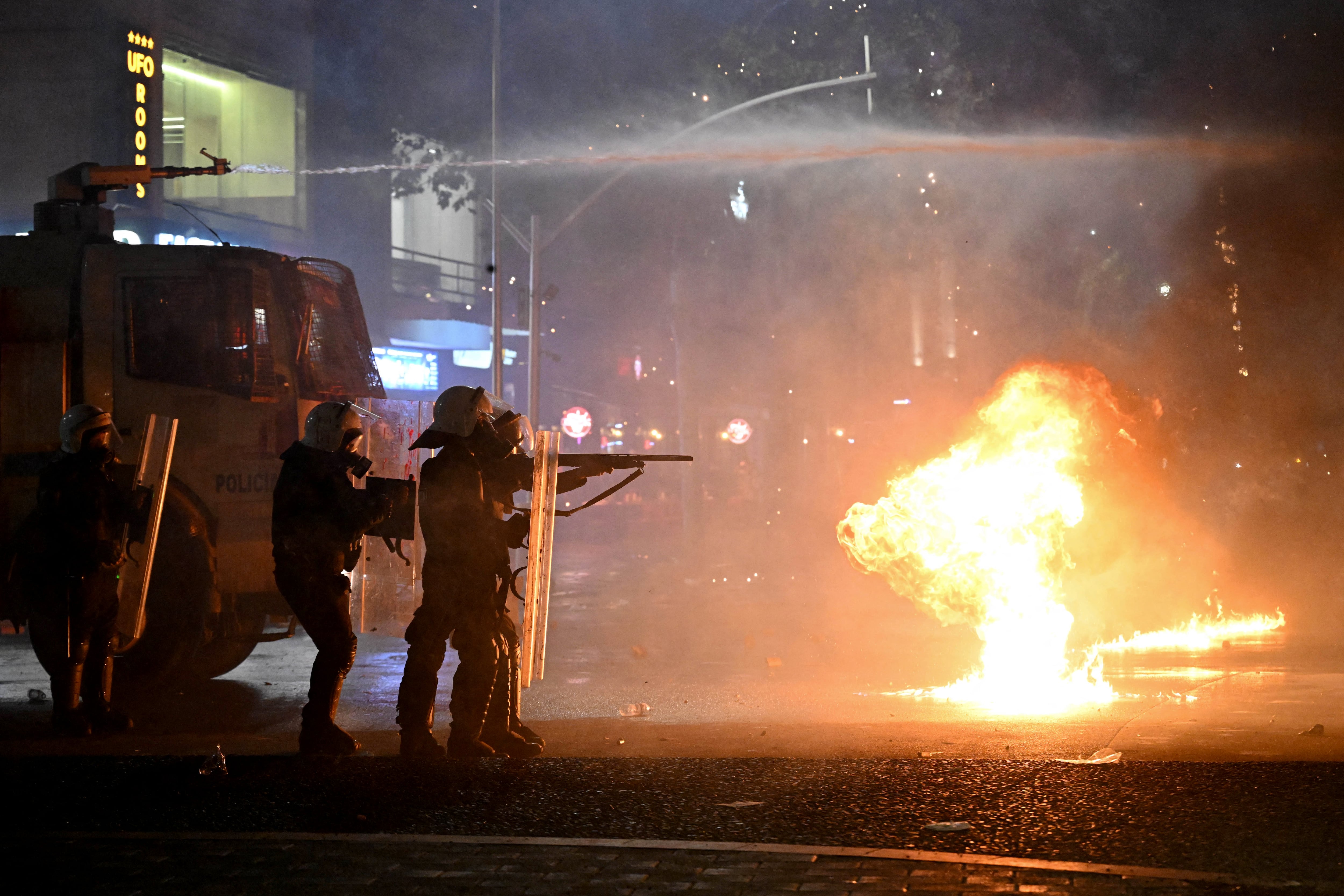 Riot police officers take cover from molotov cocktails thrown by protesters during an anti-government demonstration in central Tirana on October 18, 2026, as protests continued for a sixth consecutive day over university conditions and demands for the resignation of Albania's Prime Minister. Albanian police fired water cannon and tear gas on October 18, 2026, as violent anti-government protests entered a sixth day and Prime Minister rejected demonstrators demands that he resign. (Photo by Armend NIMANI / AFP)