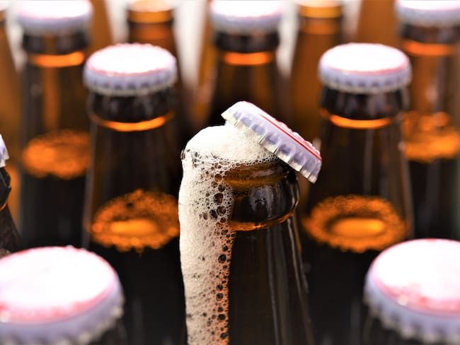Cerveza abierta botando espuma blanca, alrededor de otras botellas de cervezas selladas (Getty Images)