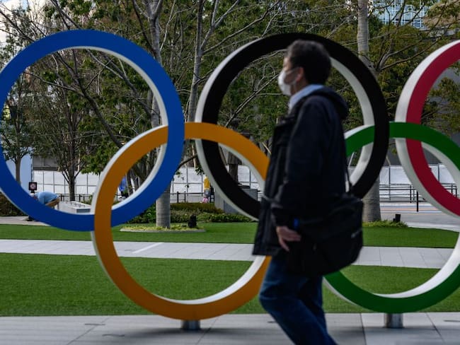 Un hombre con tapabocas camina frente a los anillos olímpicos en Tokio, Japón. 