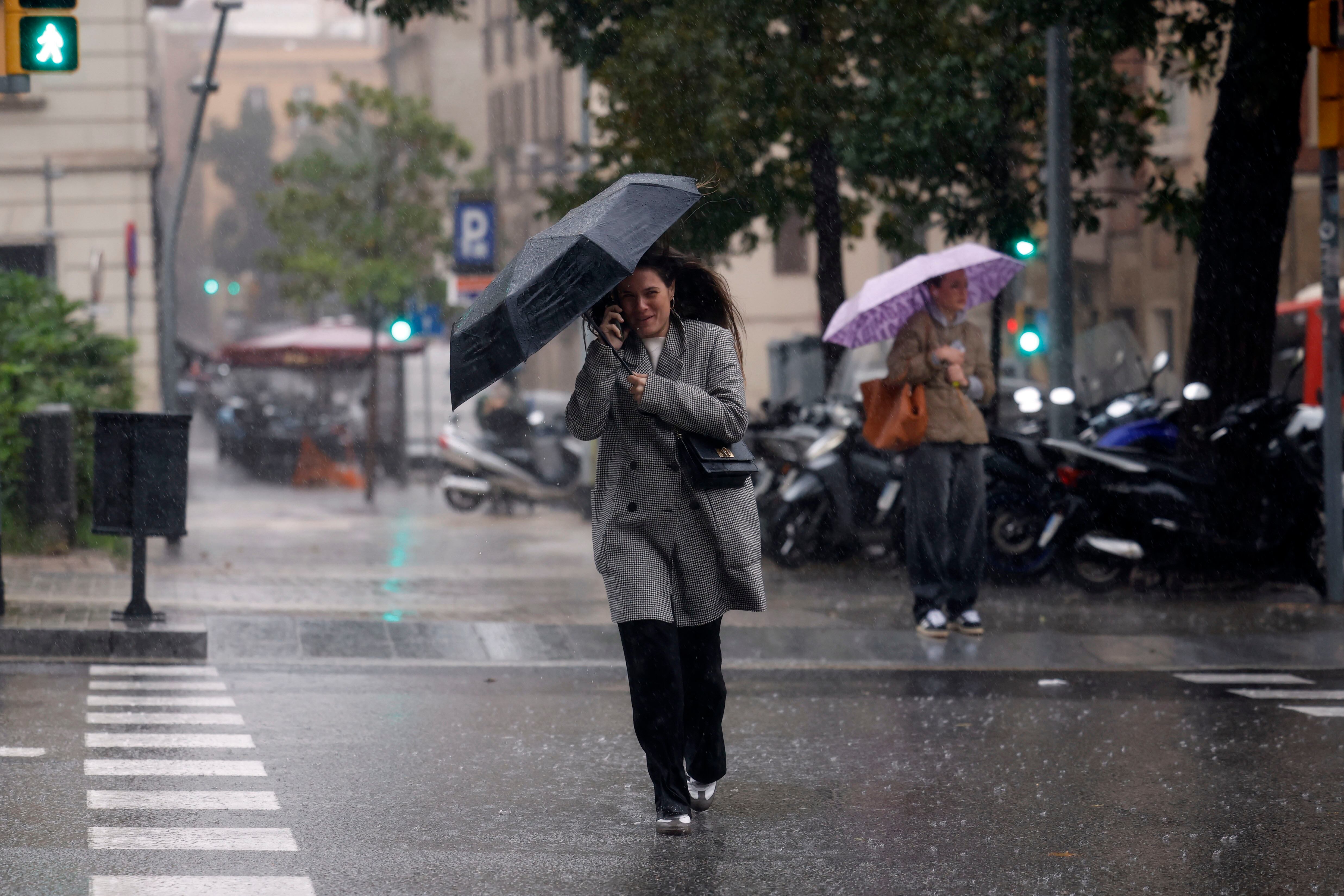GRAFCAT035. BARCELONA, 04/11/2024.- Una mujer se protege de la lluvia en el centro de Barcelona este lunes cuando las comarcas de del Garraf y del Barcelonès, en Barcelona, están en aviso rojo de la Agencia Estatal de Meteorología (Aemet),
