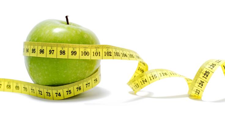 Primer plano de una manzana verde con una cinta para medir (Foto vía Getty Images)