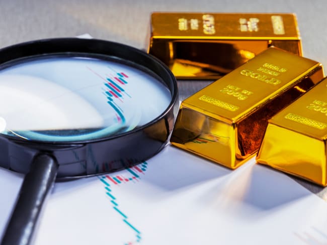 Una lupa sobre una gráfica de cifras y al lado varios lingotes de oro (Foto vía Getty Images)