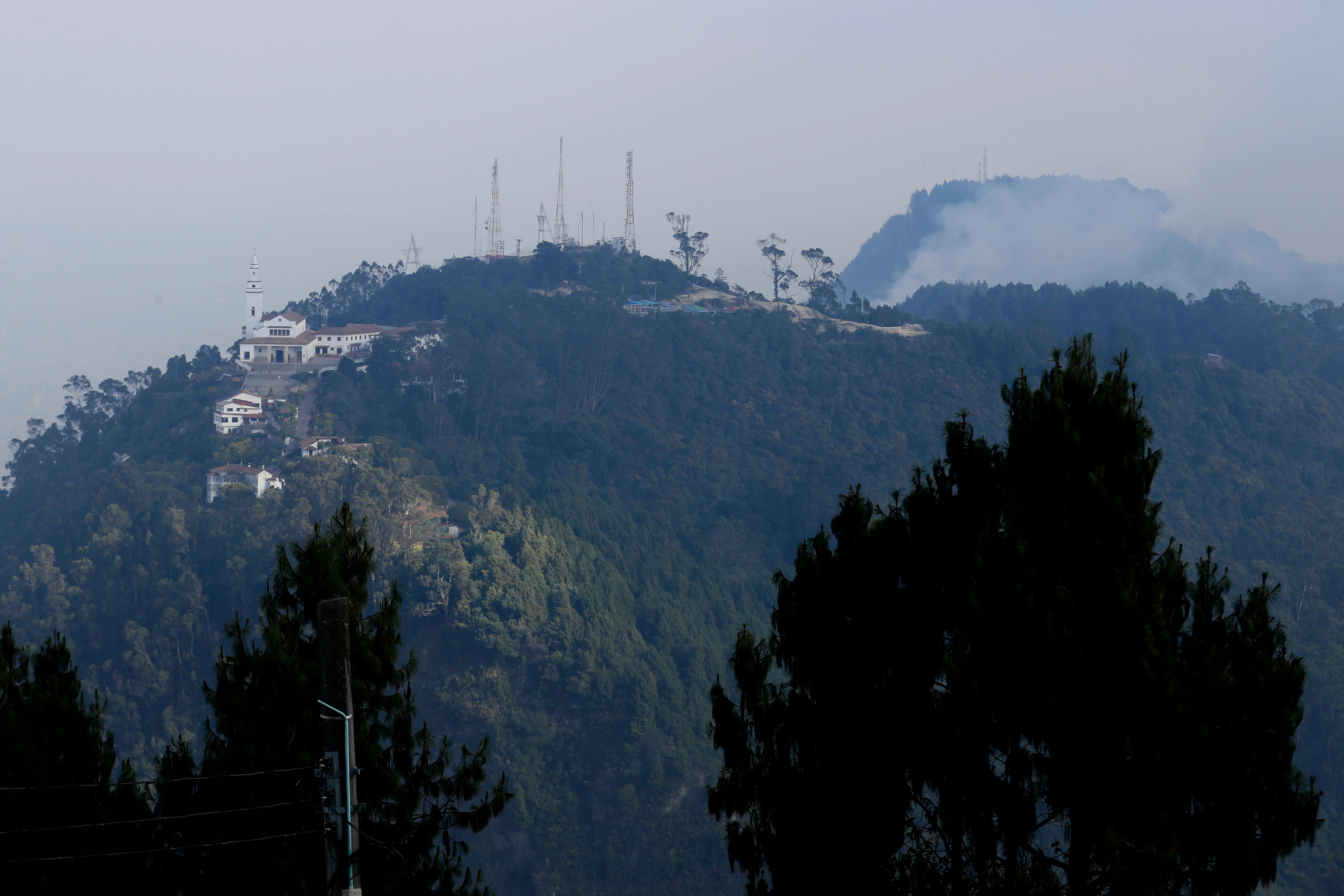 BOG400. BOGOTÁ (COLOMBIA), 27/01/2024.- Vista hoy del cerro de Monserrate bajo una capa de humo producida por un incendio forestal en el cerro El Cable (d), en Bogotá (Colombia). Frente a los incendios que golpean a la capital colombiana, el alcalde Carlos Fernando Galán anunció medidas como una alerta zonal por deterioro de la calidad del aire en el suroccidente de la ciudad, así como extender la medida de pico y placa -que restringe el tránsito de vehículos- a los sábados. EFE/ Carlos Ortega