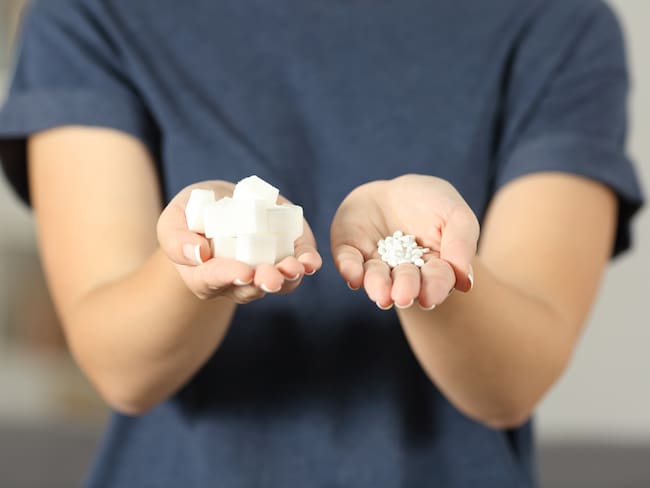 Vista frontal de cerca de las manos de una mujer sosteniendo terrones de azúcar y pastillas de sacarina en casa / Getty Images