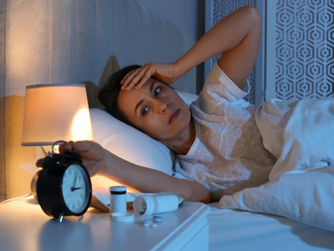 Mujer revisando el reloj, en su cama, mientras intenta conciliar el sueño (Getty Images)