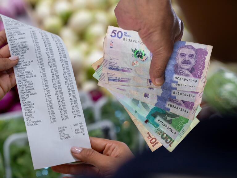 Mujer comprando en una tienda de conveniencia y revisando su recibo - Pesos colombianos en una mano (Getty Images)