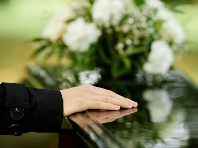 Persona colocando su mano sobre la lápida de un fallecido (Foto vía Getty Images)