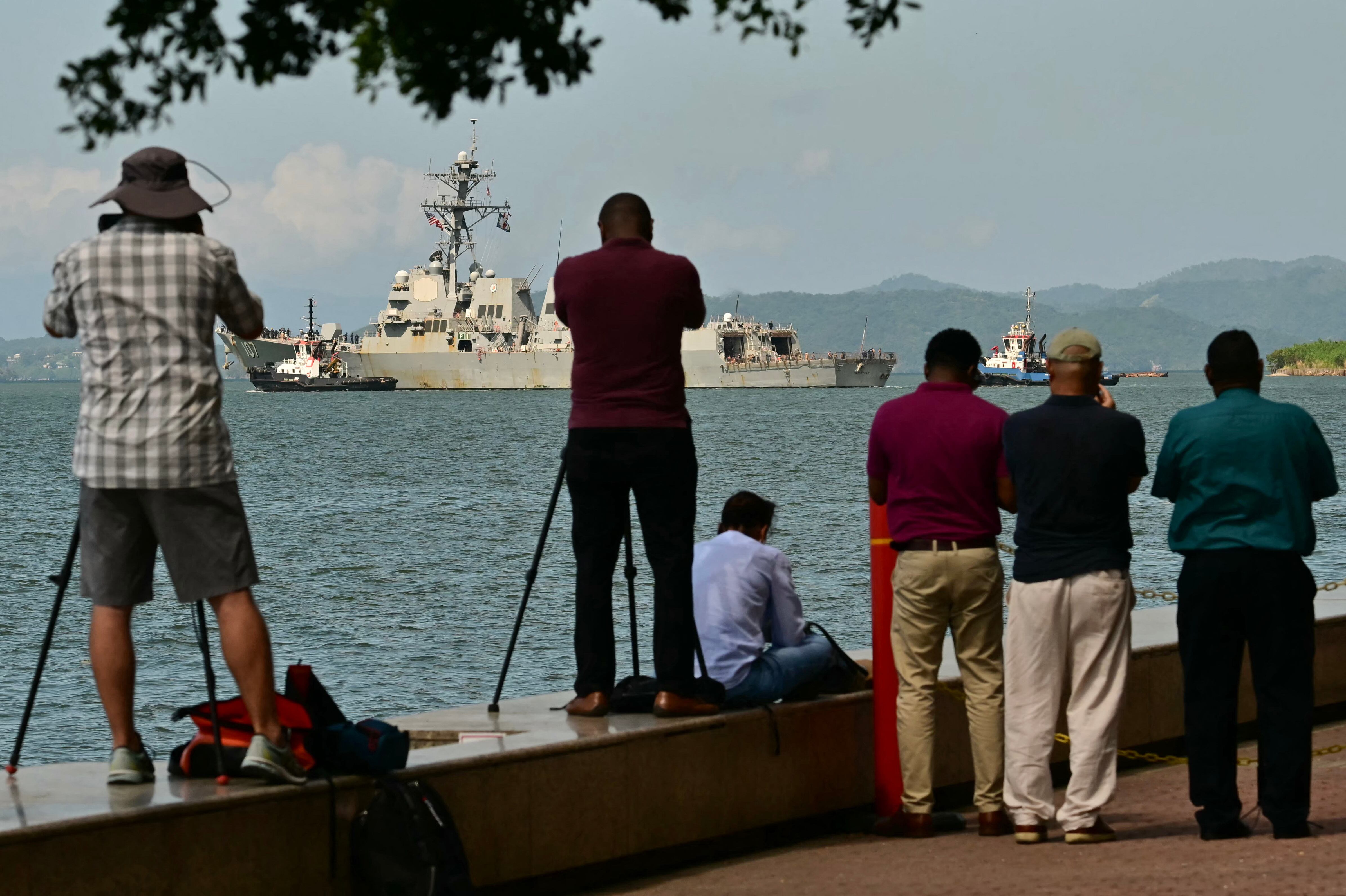 People watch and take pictures of the USS Gravely, a US Navy warship, departing the Port of Port of Spain on October 30, 2025. The US warship arrived in Trinidad and Tobago on October 26, 2025, for joint exercises near the coast of Venezuela, as Washington ratcheted up pressure on drug traffickers and Venezuelan leader Nicolas Maduro. (Photo by MARTIN BERNETTI / AFP)