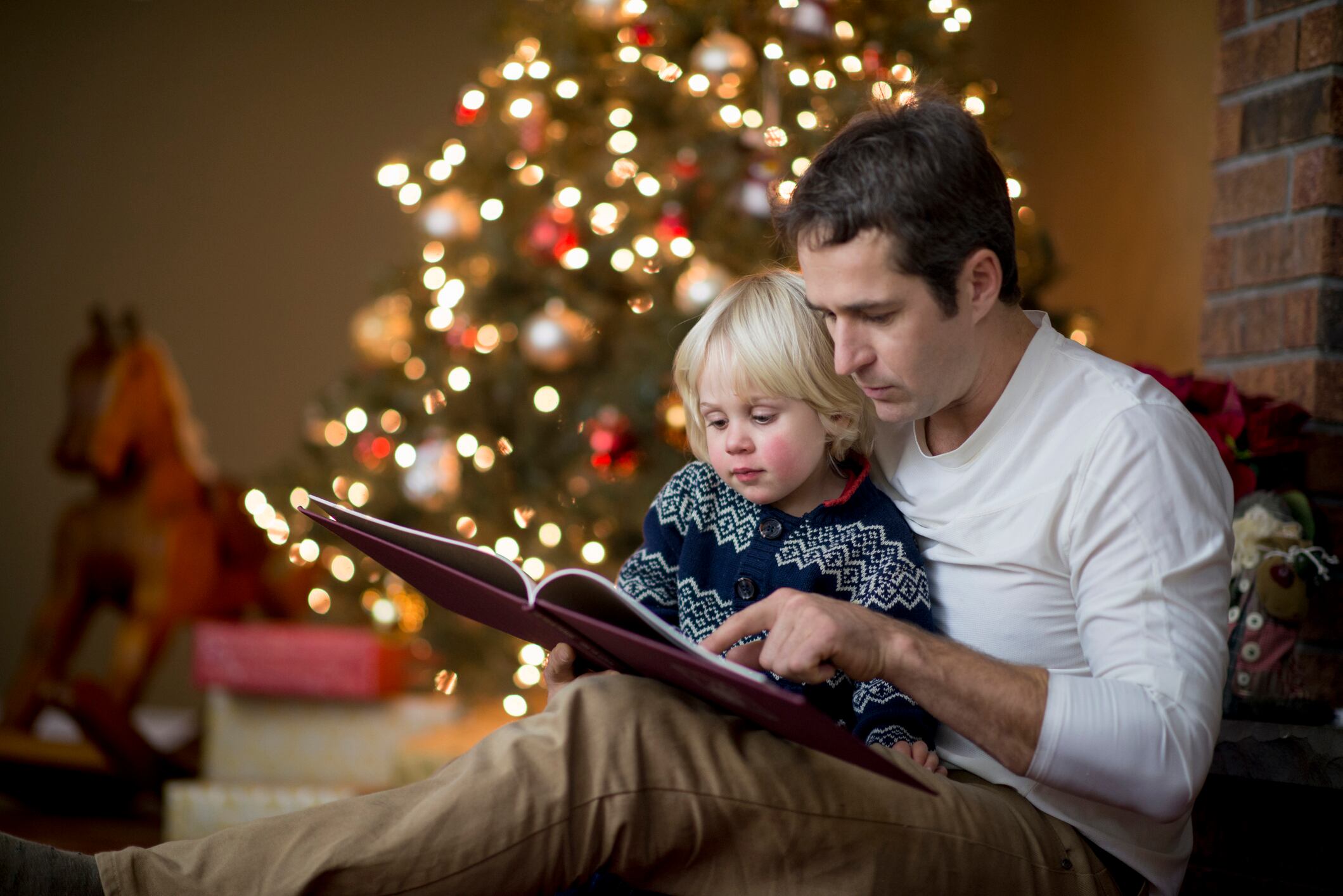 Un padre le lee un libro a su pequeño en Navidad. Vía Getty Images