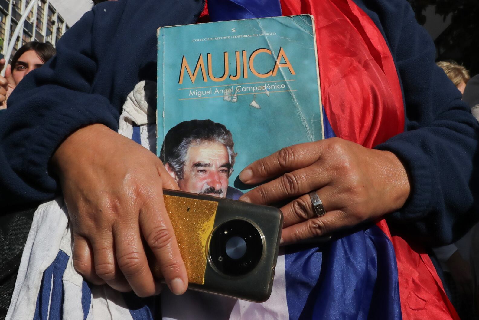 AME7514. MONTEVIDEO (URUGUAY), 14/05/2025.- Una persona sostiene un libro durante el cortejo fúnebre del expresidente uruguayo José Mujica este miércoles, en Montevideo (Uruguay). El féretro de Mujica arribó sobre las 13:15 horas (16:15 GMT) al Palacio Legislativo de Montevideo, donde será velado. EFE/ Raúl Martínez