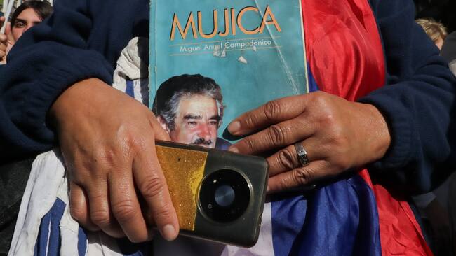 AME7514. MONTEVIDEO (URUGUAY), 14/05/2025.- Una persona sostiene un libro durante el cortejo fúnebre del expresidente uruguayo José Mujica este miércoles, en Montevideo (Uruguay). El féretro de Mujica arribó sobre las 13:15 horas (16:15 GMT) al Palacio Legislativo de Montevideo, donde será velado. EFE/ Raúl Martínez