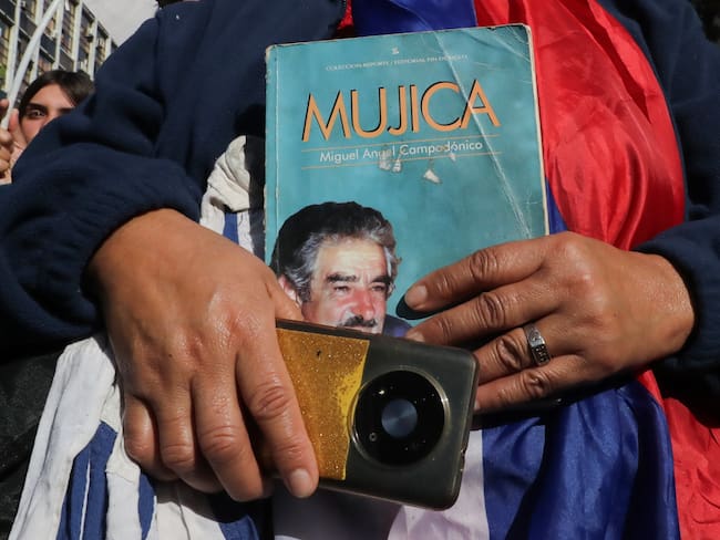 AME7514. MONTEVIDEO (URUGUAY), 14/05/2025.- Una persona sostiene un libro durante el cortejo fúnebre del expresidente uruguayo José Mujica este miércoles, en Montevideo (Uruguay). El féretro de Mujica arribó sobre las 13:15 horas (16:15 GMT) al Palacio Legislativo de Montevideo, donde será velado. EFE/ Raúl Martínez