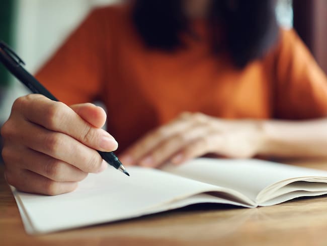 Mujer usando un esfero o bolígrafo para escribir en un cuaderno (Foto vía GettyImages)