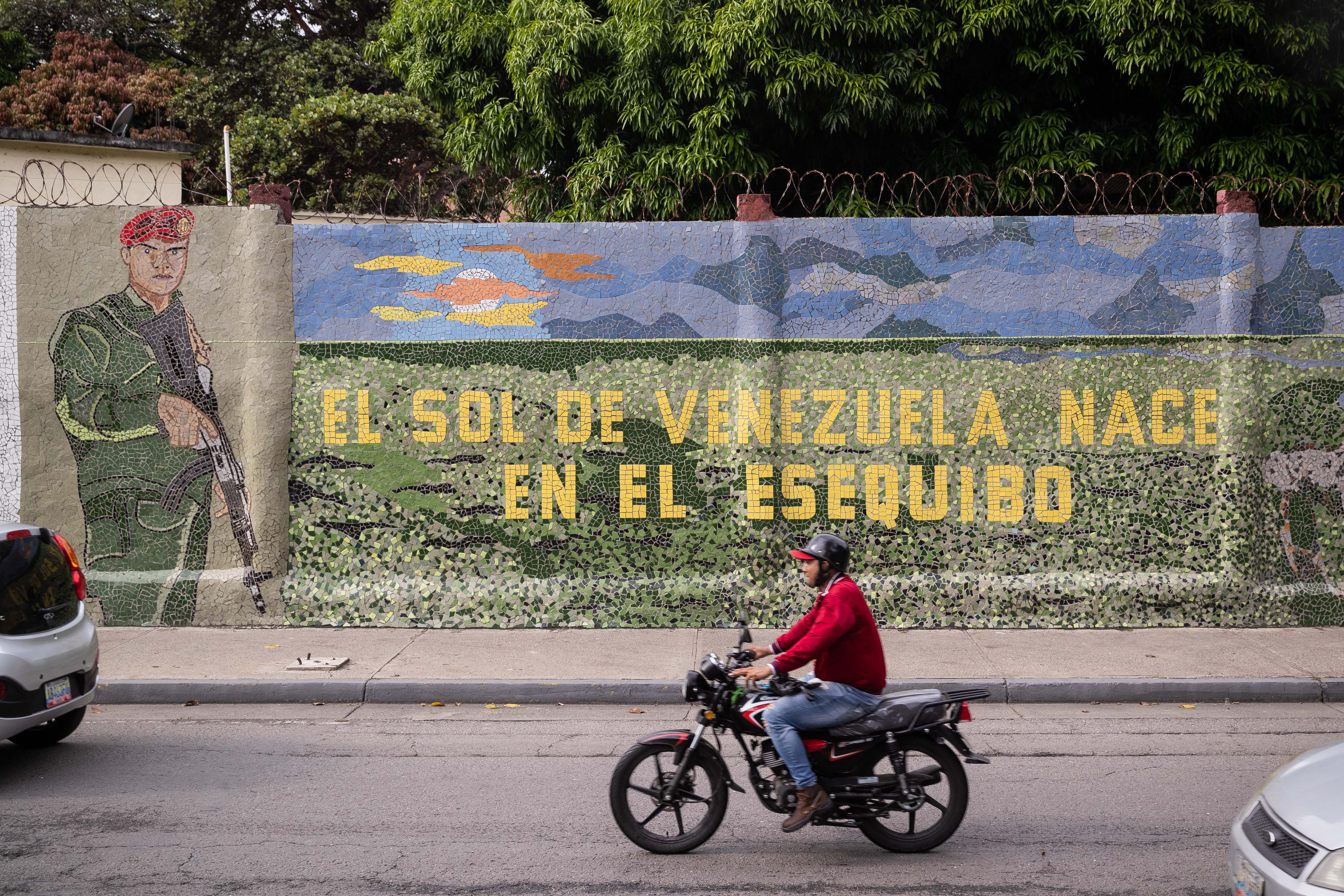 AME3693. CARACAS (VENEZUELA), - Un hombre conduce una moto frente a un mural que dice "El sol de Venezuela nace por el esequibo", en Caracas (Venezuela).. EFE/ Rayner Peña R.