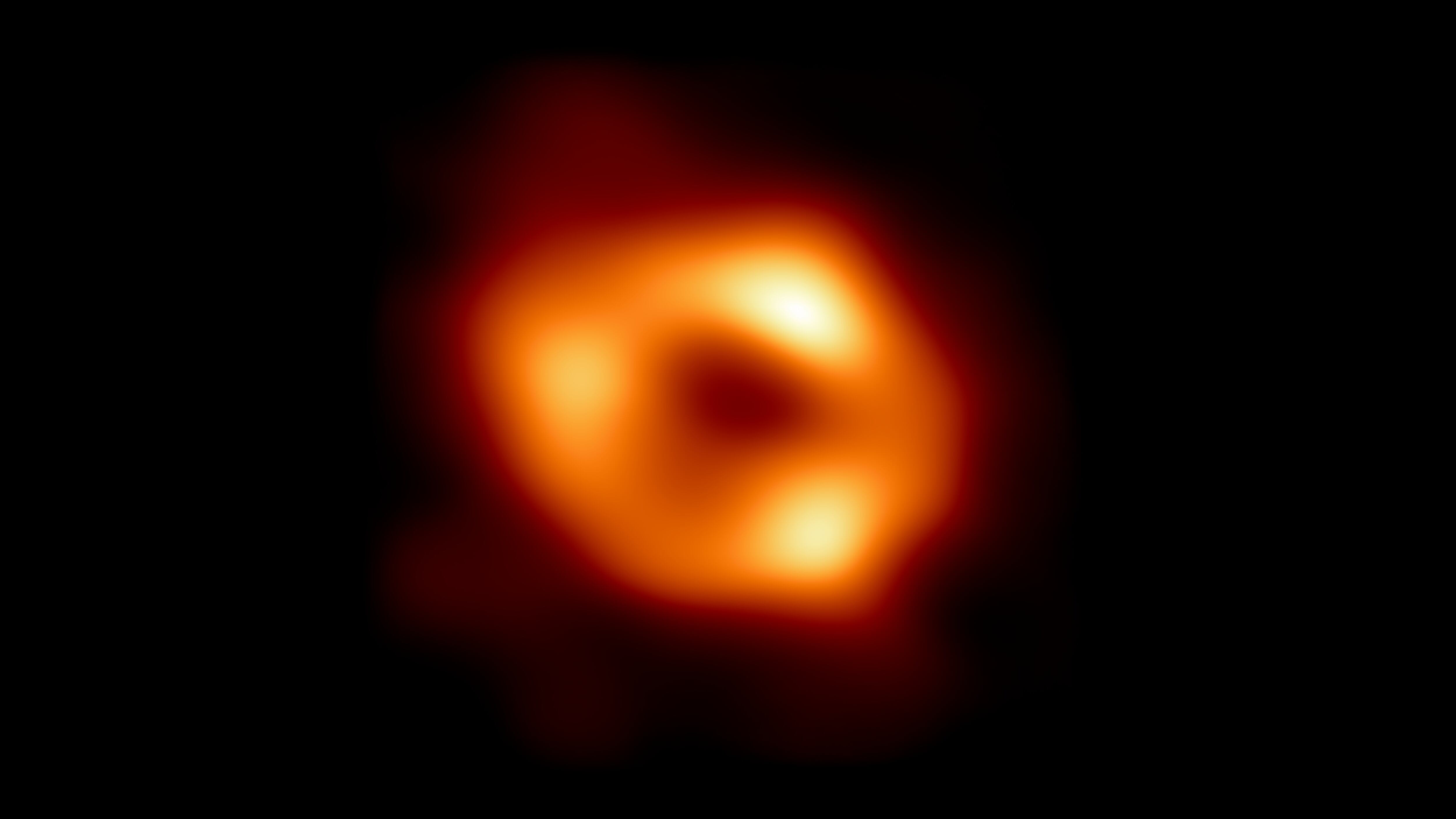 IN SPACE -  MAY 12: In this handout photo provided by NASA,  This is the first image of Sgr A*, the supermassive black hole at the centre of our galaxy, with an added black background to fit wider screens. It's the first direct visual evidence of the presence of this black hole. It was captured by the Event Horizon Telescope (EHT), an array which linked together eight existing radio observatories across the planet to form a single Earth-sized virtual telescope. The telescope is named after the event horizon, the boundary of the black hole beyond which no light can escape.   The image of the Sgr A* black hole is an average of the different images the EHT Collaboration has extracted from its 2017 observations.  In addition to other facilities, the EHT network of radio observatories that made this image possible includes the Atacama Large Millimeter/submillimeter Array (ALMA) and the Atacama Pathfinder EXperiment (APEX) in the Atacama Desert in Chile, co-owned and co-operated by ESO is a partner on behalf of its member states in Europe. (Photo by NASA Via Getty Images)