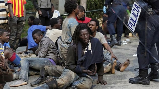 Migrantes sentados en el suelo junto a policías españoles tras cruzar una cerca para entrar en el enclave español de Ceuta, en España, el viernes 17 de febrero de 2017. Foto: Associated Press - AP