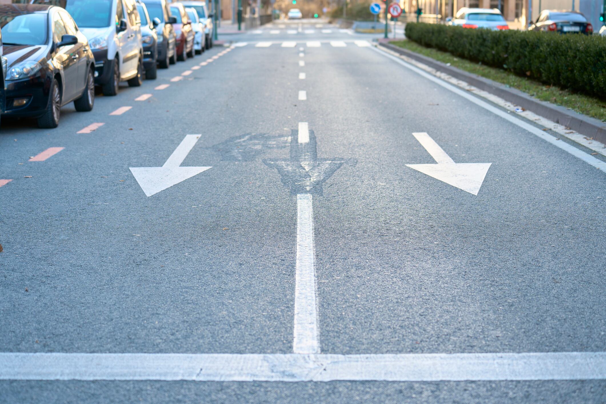 Front view of a street with traffic signs and traffic lights, on the left there are cars in a row.