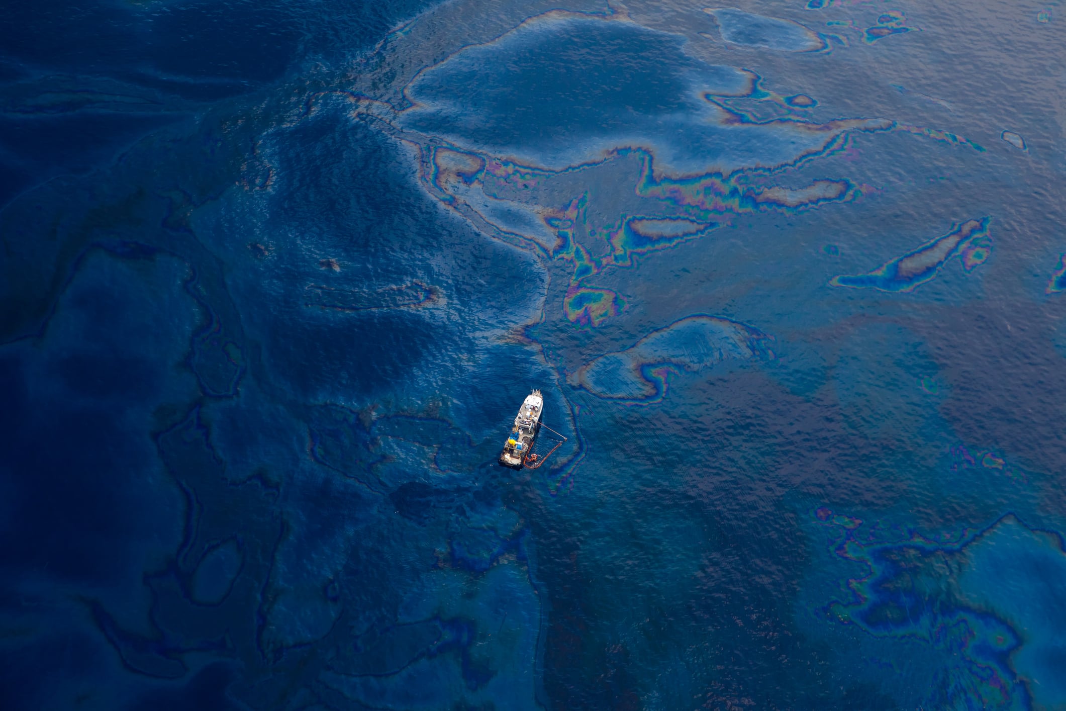 Aerial view from a seaplane. small white boat is seen floating atop oil covered waters of the Gulf of Mexico. the ocean water is a deep blue and teal color.  