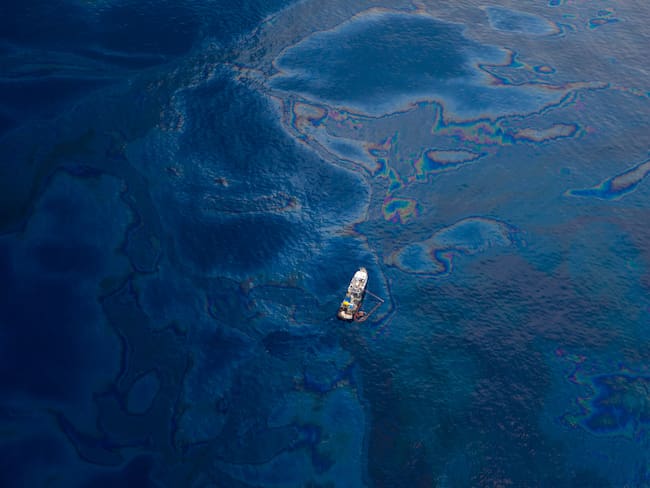 Aerial view from a seaplane. small white boat is seen floating atop oil covered waters of the Gulf of Mexico. the ocean water is a deep blue and teal color.  
