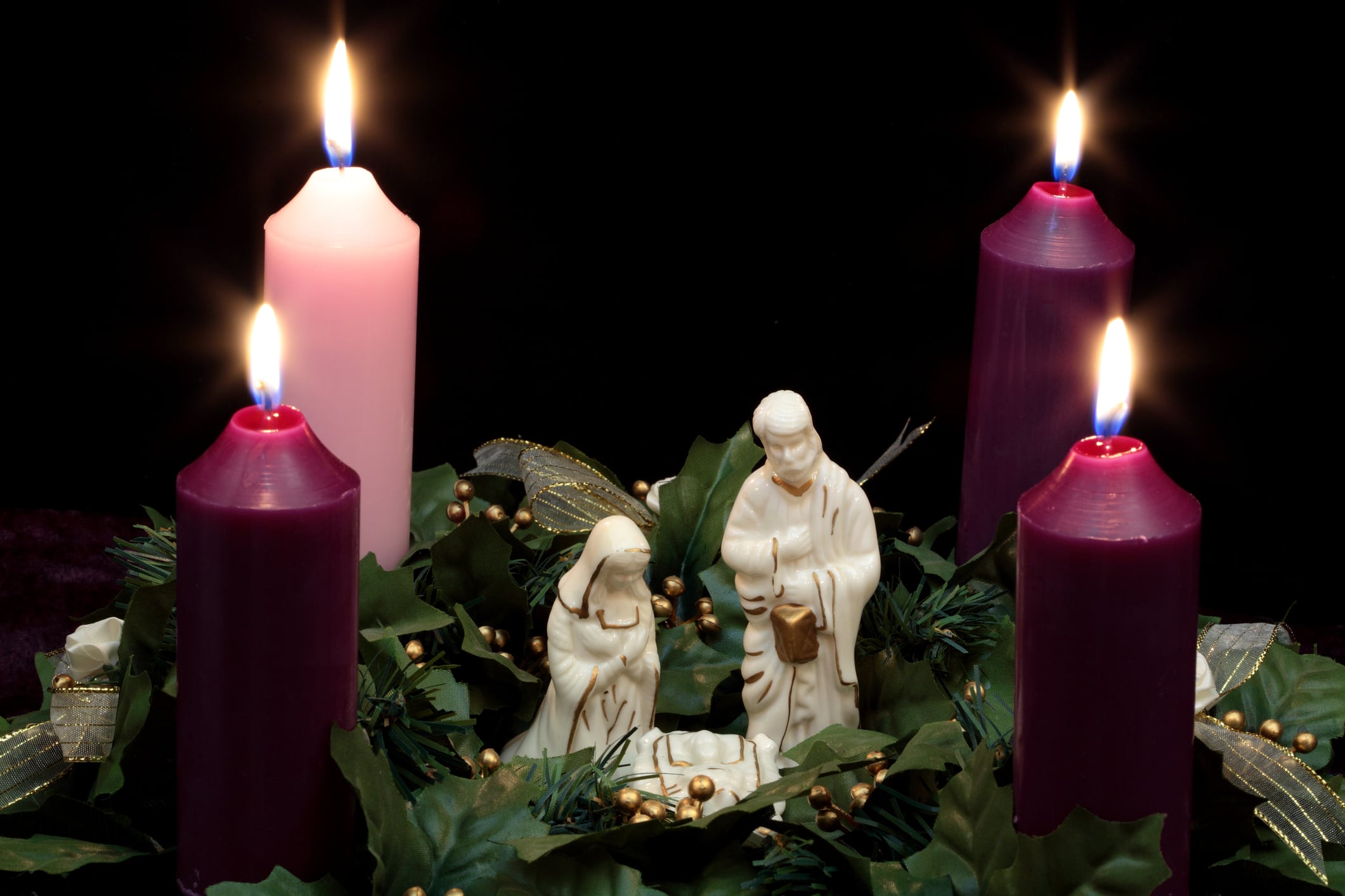 Corona de Adviento con belén en medio de 4 velas encendidas y vegetación de acebo. La imagen horizontal sería buena para uso navideño cristiano o religioso.  / Getty Images