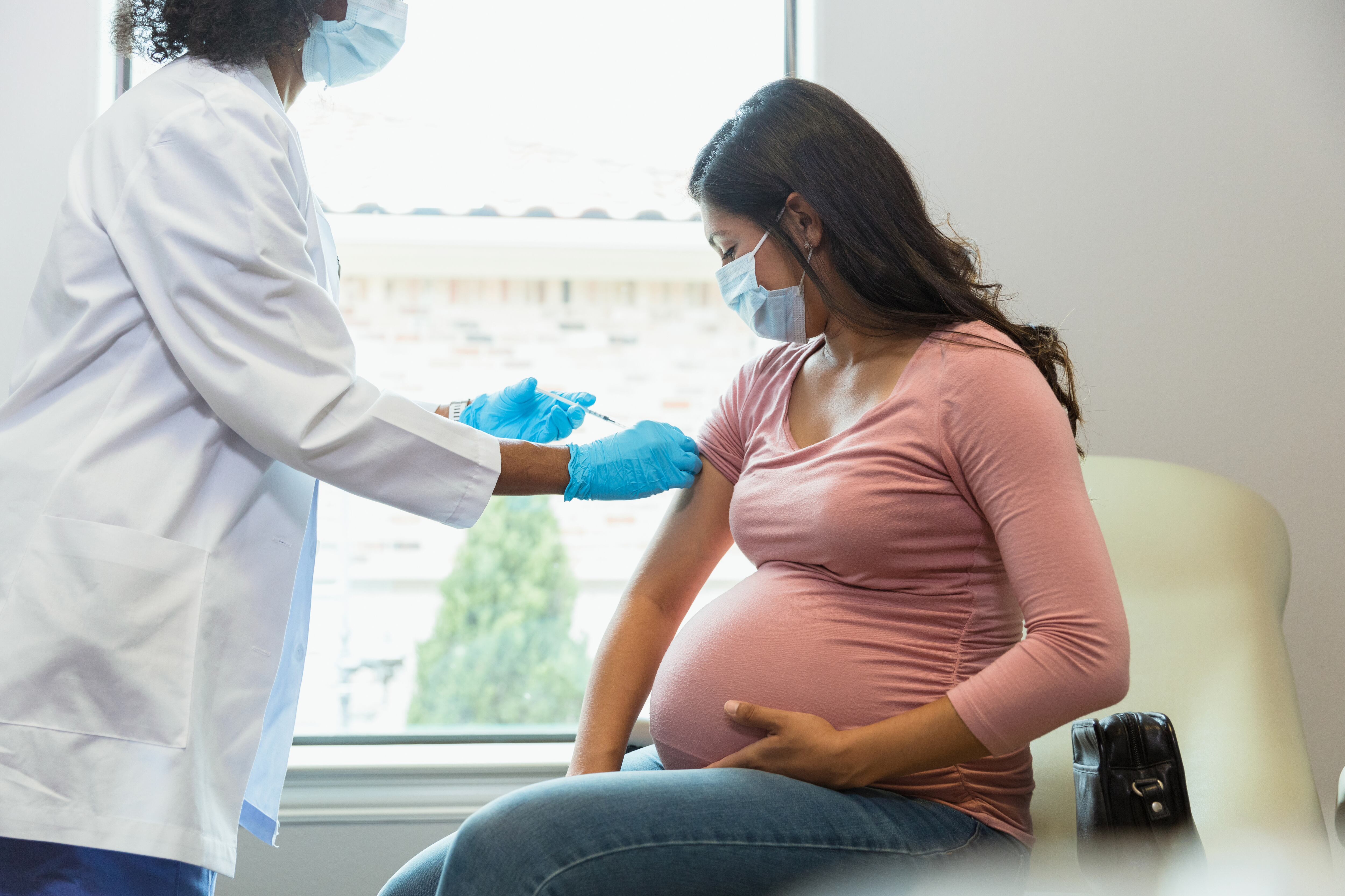 Pregnant woman watches as the female technician administers a booster shot.