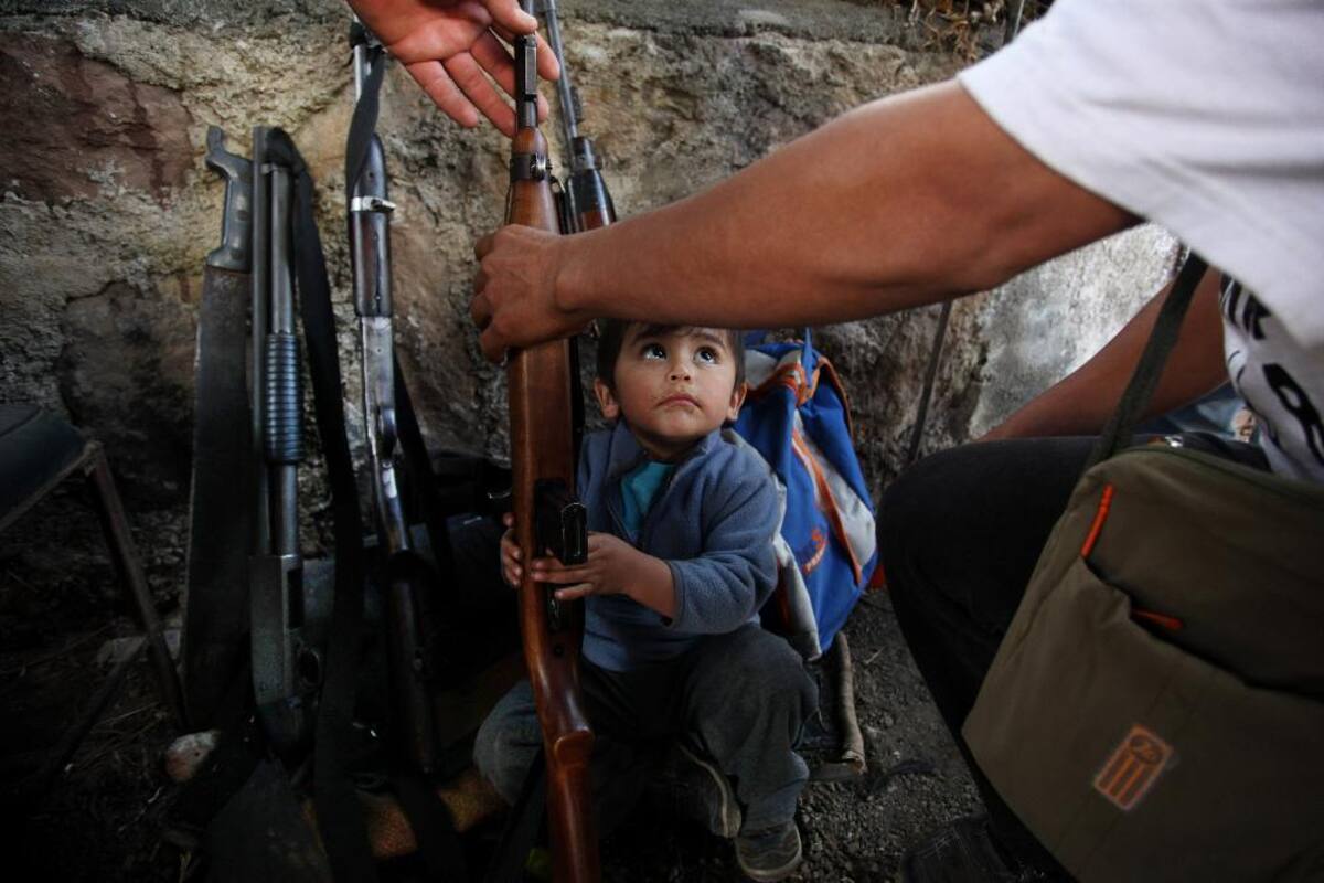 16 de enero 2014. Un niño trata de ayudar a su padre a organizar las armas en un puesto de control establecido por el Consejo de Autodefensa de Michoacán, México.