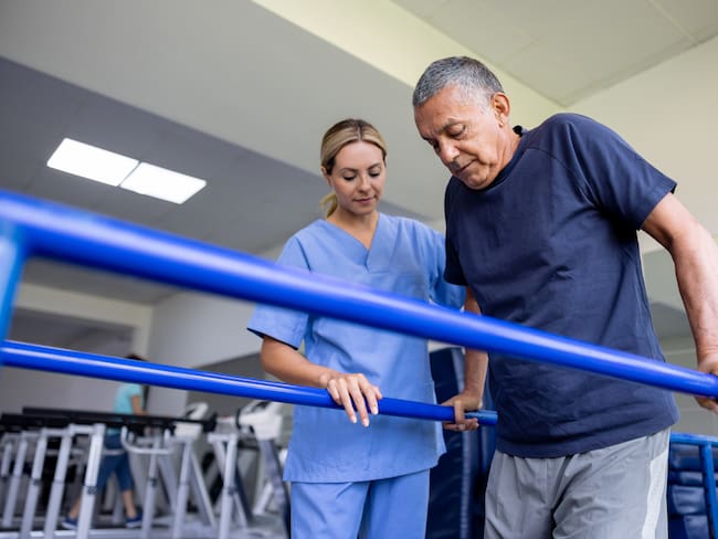 Latin American man doing physical therapy and walking on bars with the assistance of his physical therapist
